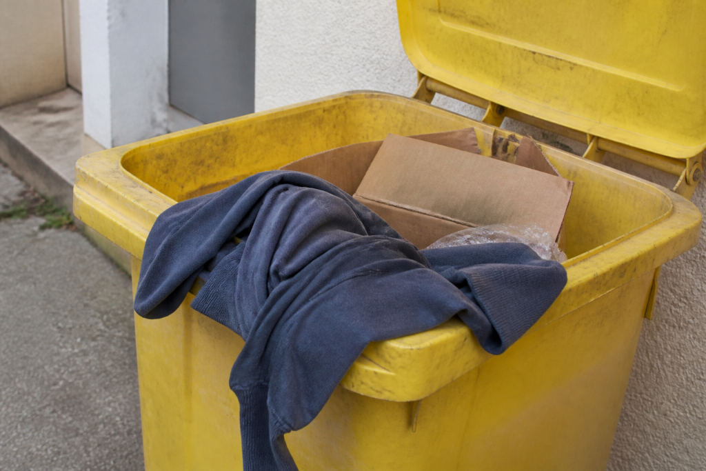 Poubelle jaune ouverte avec un vetement et des cartons