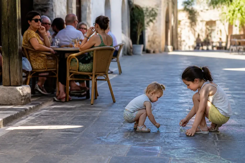 Tables de cafe ensoleillees, enfants jouant sur le dallage